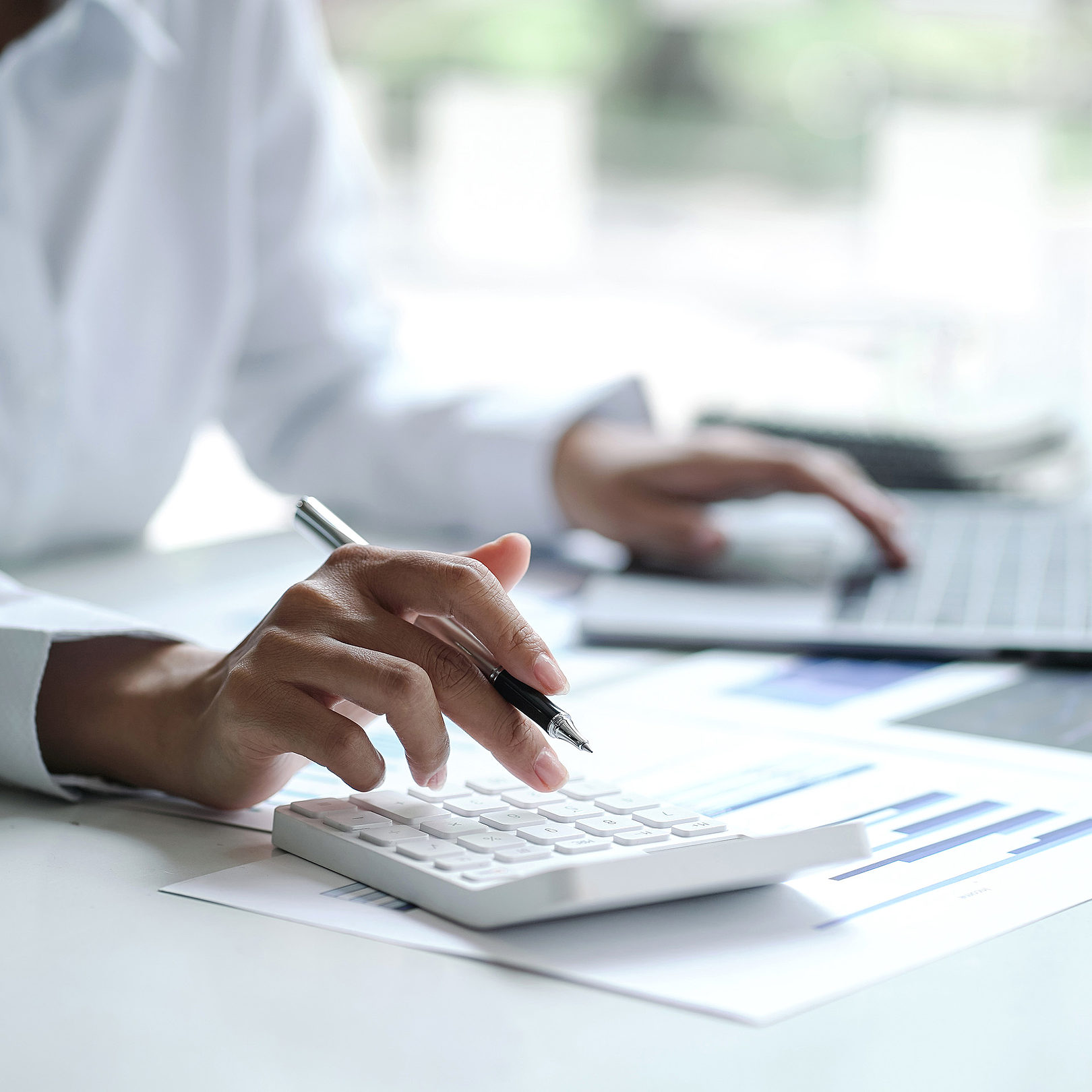 person using a calculator on a white desk with sheets of printed data sets