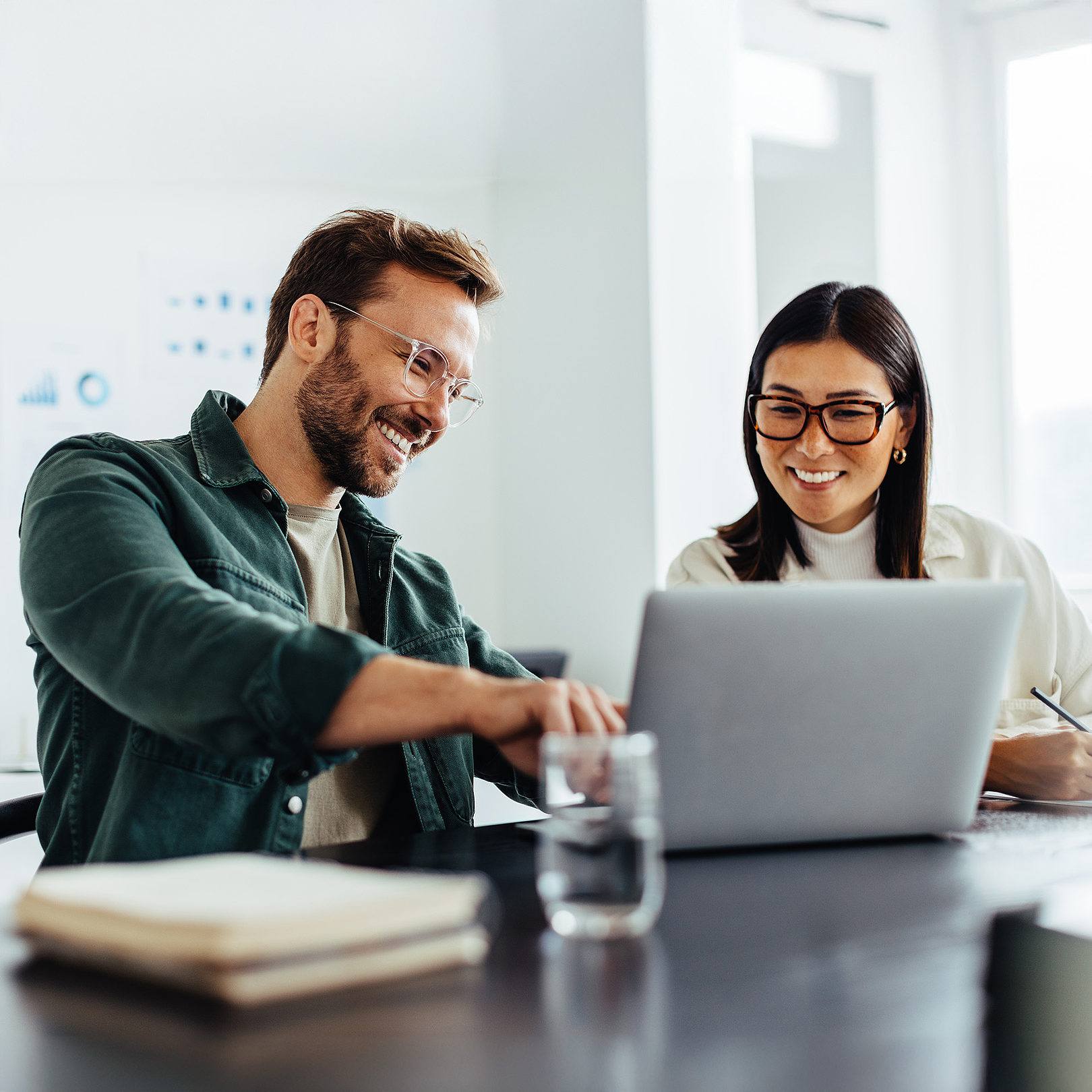 Two business people are sitting at a desk together looking at a laptop